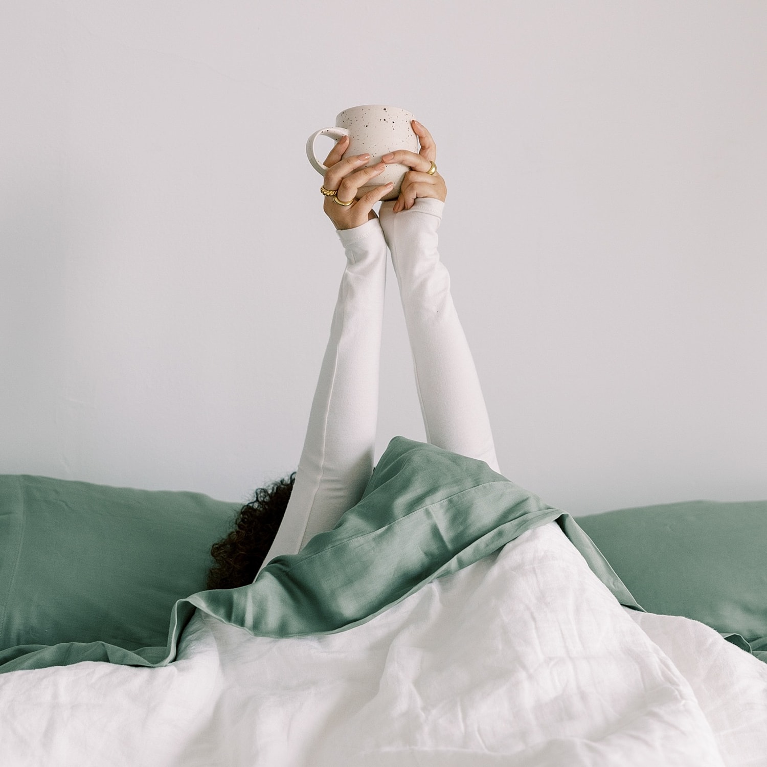 Person in bed holding a mug happily.